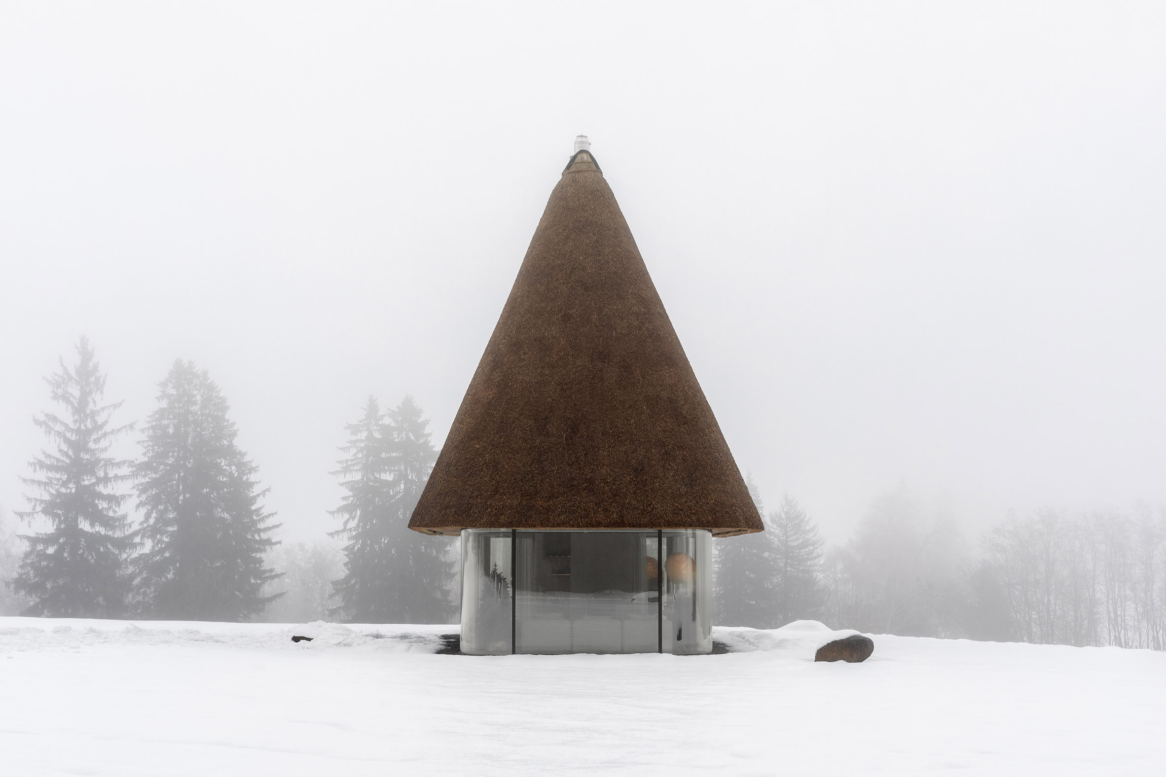 Glass hut with thatched roof in snowy landscape