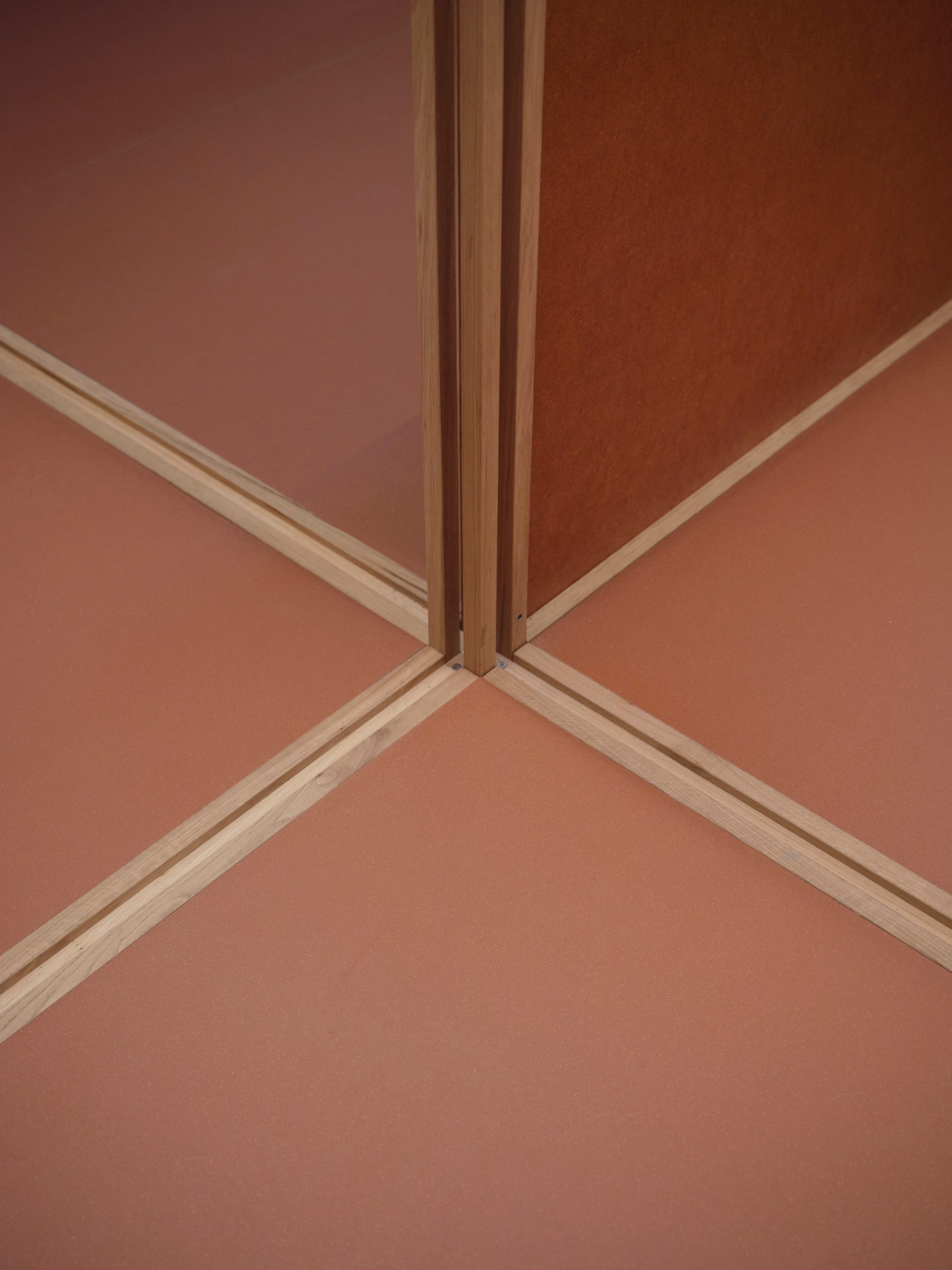 Close-up photo of timber beams and posts joing with red-toned floor and wall panels in the QuadroDesign Salone 2026 stand